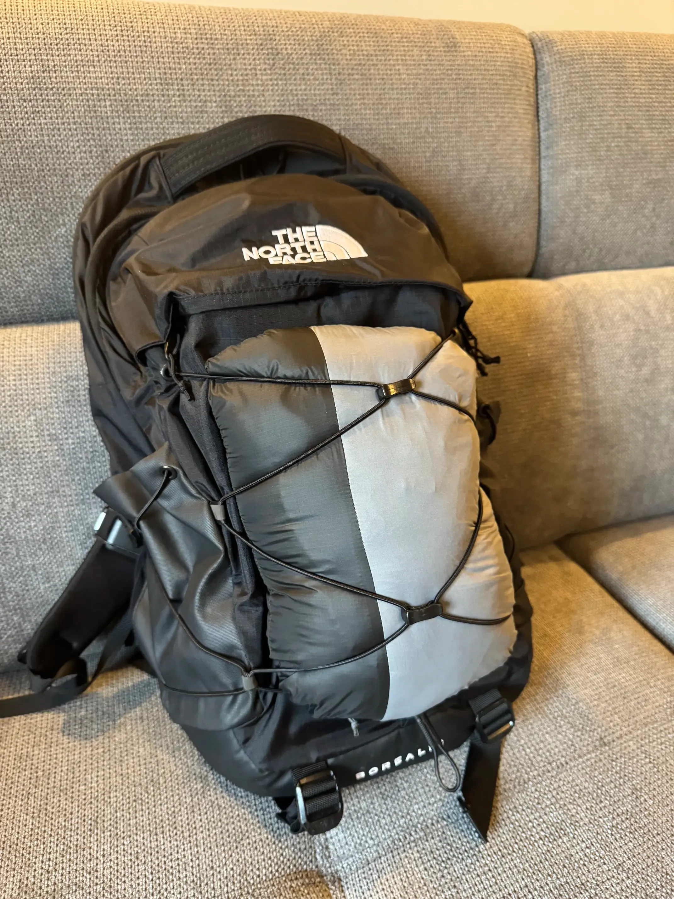 A photo of a backpack with a folded jacket entangled in the elastic straps on the backpack's back.