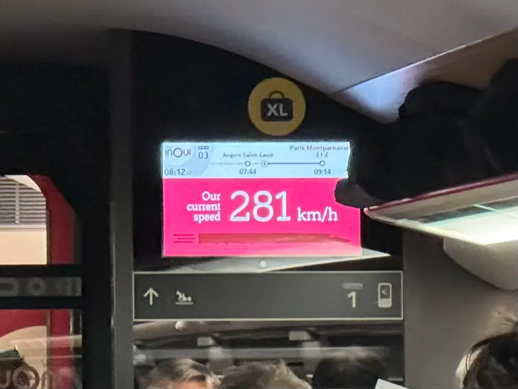 A photo of a screen in a train car. The screen reads "Our current speed 281 km/h."